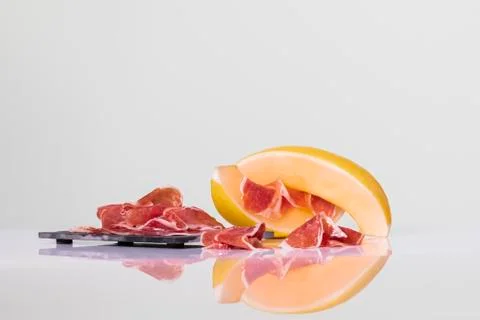 Thin cured ham slices on a dark plate next to melon slices with some more cur Stock Photos