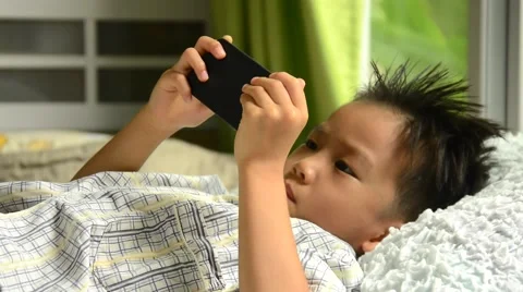 Thin focus on hand of sleepy young Asian boy using cellphone on white bed Vídeos de archivo 53356200