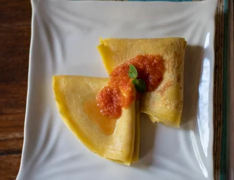 Thin folded pancake served on the table with tomato sauce in a white plate fo Stock Photos