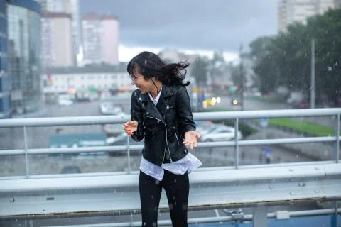 A thin girl in black dodges the gusts of wind and rain. Stock Photos