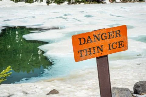 Thin ice warning notice on orange danger signboard by mountain lake Stock Photos