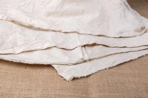 A thin light-colored fabric lies in several layers on a burlap. Stock Photos