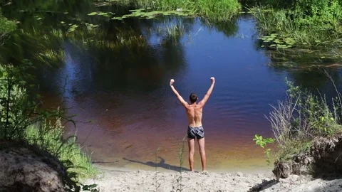 Thin man doing exercises on the shore of wild river Stock Footage