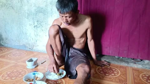 A thin man eating on the floor of his simple rural house. Stock Footage 317935429
