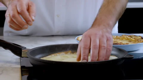 A thin pancake is being cooked in a pan, the cook moves the pan over the stove. Stock Footage 276282759