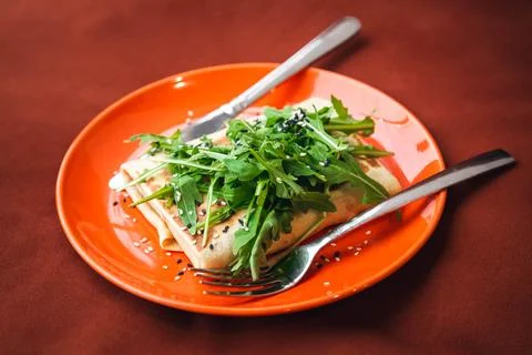 Thin pancake with meat inside, decorated with herbs on a bright orange plate. Stock Photos
