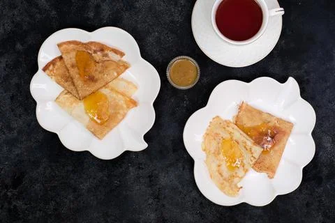 Thin pancakes with appricot jam on white ceramic plates with cup of tea on black Foto stock