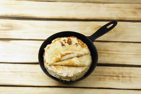 Thin pancakes in a rustic black frying pan on a wooden background. Stock Photos