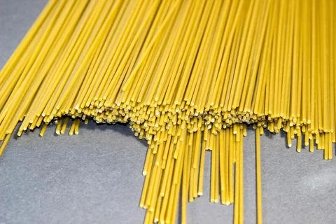 Thin raw spaghetti is scattered on a dark background. Stock Photos