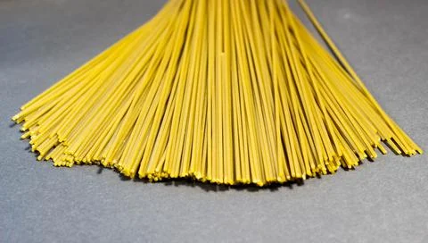Thin raw spaghetti is scattered on a dark background. Stock Photos