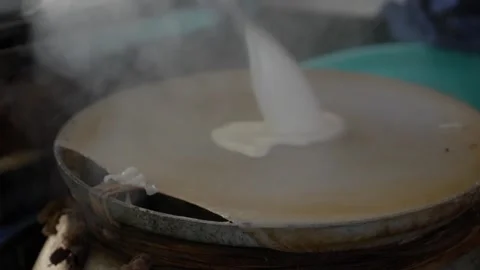 Thin rice batter spreads on a round steaming surface while cooking over heat in 库存影片 331011343