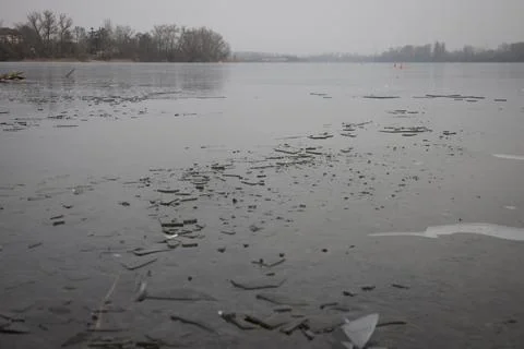 Thin shards of broken ice float on the surface of a calm lake during a gray w Foto stock