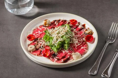 Thin-sliced beef carpaccio served with greens, cheese, and cherry tomatoes Stock Photos