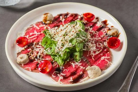 Thin-sliced beef carpaccio served with greens, cheese, and cherry tomatoes Stock Photos