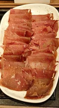 Thin slices of cured meat arranged in overlapping layers on a white plate 库存照片
