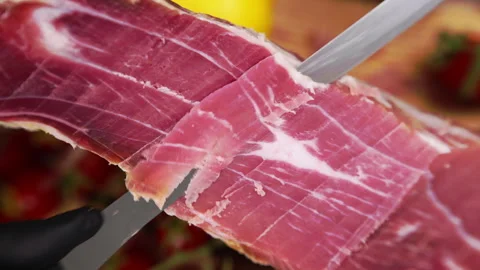 Thin slices of dry-cured prosciutto in close-up, process of delicacy slicing for Stockbeeldmateriaal 302404790