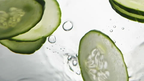 Thin slices of fresh cucumber fall down into clear water Stock Footage 153064762