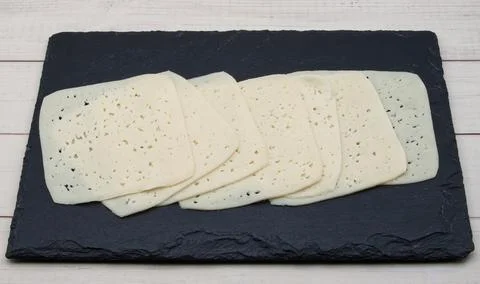 Thin slices of pale yellow cheese with small eyes are neatly stacked. Stock Photos