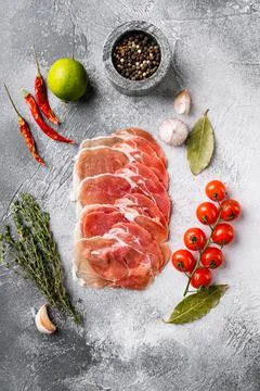 Thin slices of prosciutto, on gray stone table background, top view flat lay Stock Photos