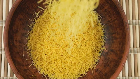 Thin small pasta is poured into a brown ceramic bowl against a bamboo mat.  Stock Footage 304391737