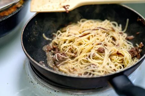 Thin spaghetti with tender chunks of stewed beef is being heated in a skillet Stock Photos