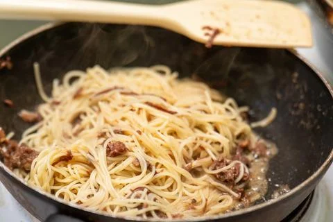 Thin spaghetti with tender chunks of stewed beef is being heated in a skill.. Stock Photos