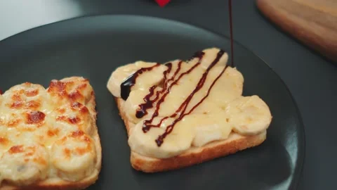A thin stream of chocolate sauce pours over a sandwich of toasted bread and Video stock 249710411