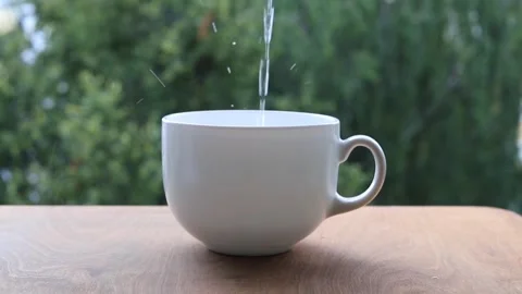 Thin stream of clear water pouring into a white porcelain cup Stock Footage 341950679
