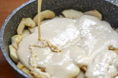 Thin stream of liquid batter being poured over apple layer in a pan for mak.. Stock Photos