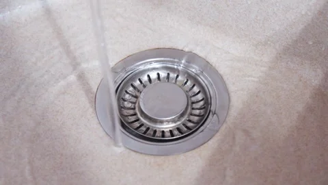 A thin stream of water flows into a kitchen sink, directed straight into th.. Video stock 314580548