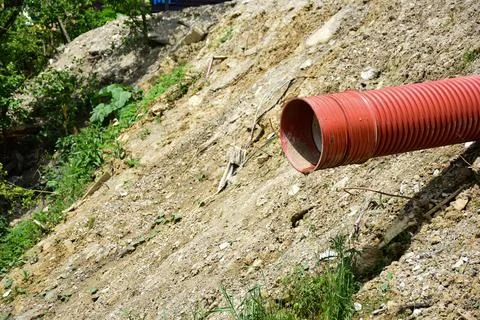 A thin stream of water flows out of a red plastic sewer pipe against Stock Photos