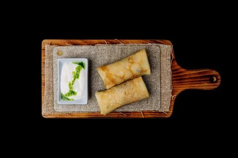 Thin stuffed pancakes or russian blini with sour cream. On a wooden board. To Stock Photos