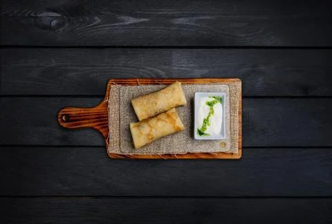 Thin stuffed pancakes or russian blini with sour cream. On a wooden board. To Stock Photos