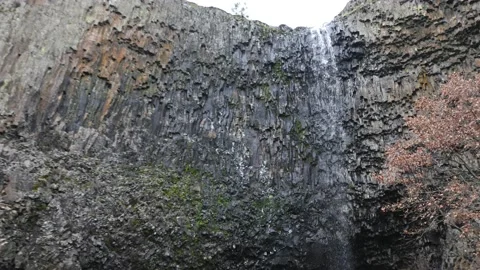 Thin tall waterfall showering off the edge of a angular rocky cliff slow mot Stock Footage 146224505