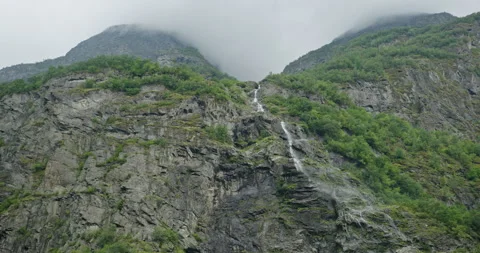 Thin waterfall on steep fjord cliffs, low clouds near Flam, Norway Video stock 321319568