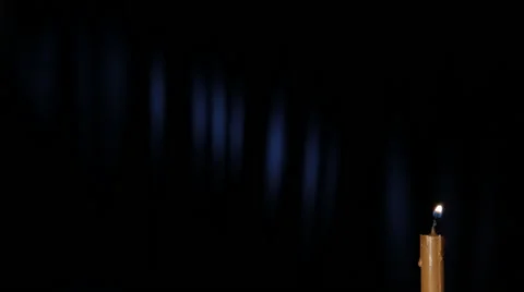 Thin wax candle is lit and burning on a black background with a blue ray Stock Footage 46952969