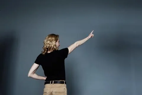 A thin young man with long blonde hair in a black T-shirt and beige jeans, st Stock Photos