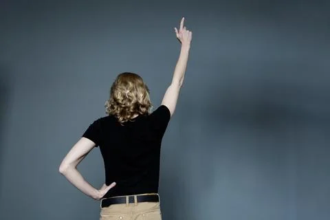 A thin young man with long blonde hair in a black T-shirt and beige jeans, st Stock Photos