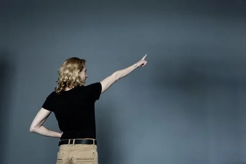 A thin young man with long blonde hair in a black T-shirt and beige jeans, st Stock Photos