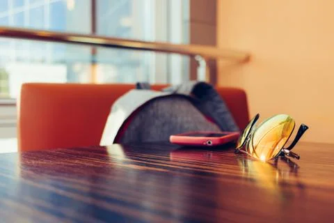 Things on a table in a cafe: sun glasses, pink smart phone and a backpack 库存照片