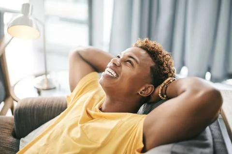 Think, man and stretching on couch, home or stress relief in lounge, happiness Stock Photos