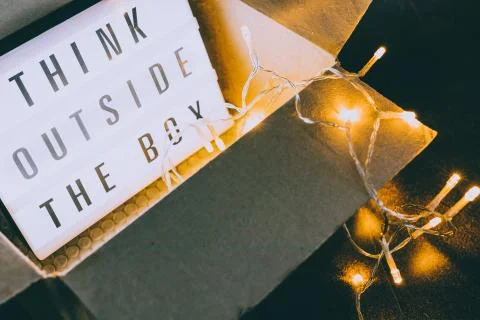 Think outside the box message on lightbox coming out of a parcel with fairy l 库存照片