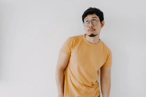 Thinking and thoughtful face of asian man in yellow t-shirt isolated on white Foto stock