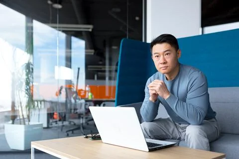 A thinking Asian man works at a computer in a modern office, a freelancer is  Foto stock