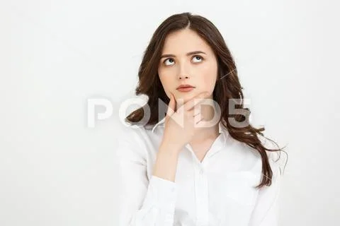 Thinking Caucasian business woman with hand on her chin and looking up on grey Stock Photos