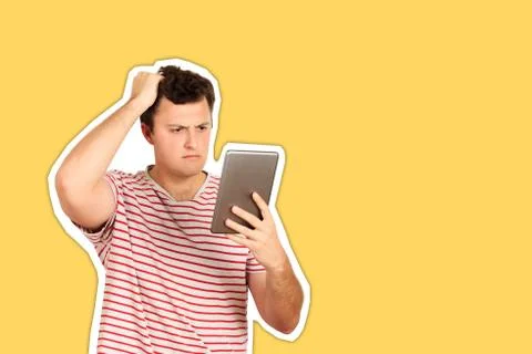 Thinking guy looks at the tablet and scratches his head with his hand. emotio Fotos de archivo