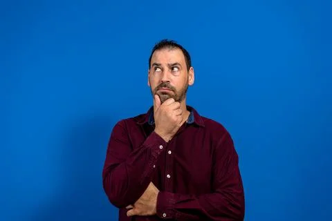 Thinking man isolated on blue background. Closeup portrait of a casual young  Stock Photos