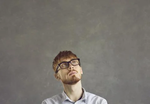 Thinking nerd man freelance programmer looking up over grey studio copy space 스톡 사진