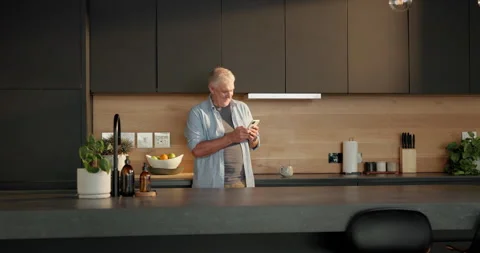 Thinking, phone and senior man in kitchen for texting, reading message and Stock Footage 336857489