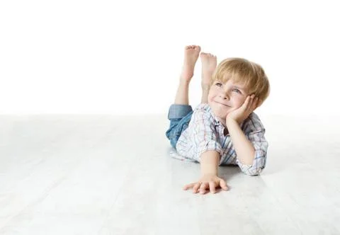 Thinking smiling little boy lying down on floor and looking up to the side Stock Photos